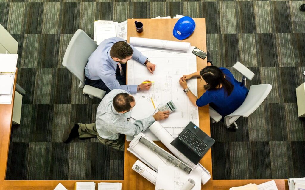 A top-down view of three people working on blueprints for a project financed with a California construction loan.