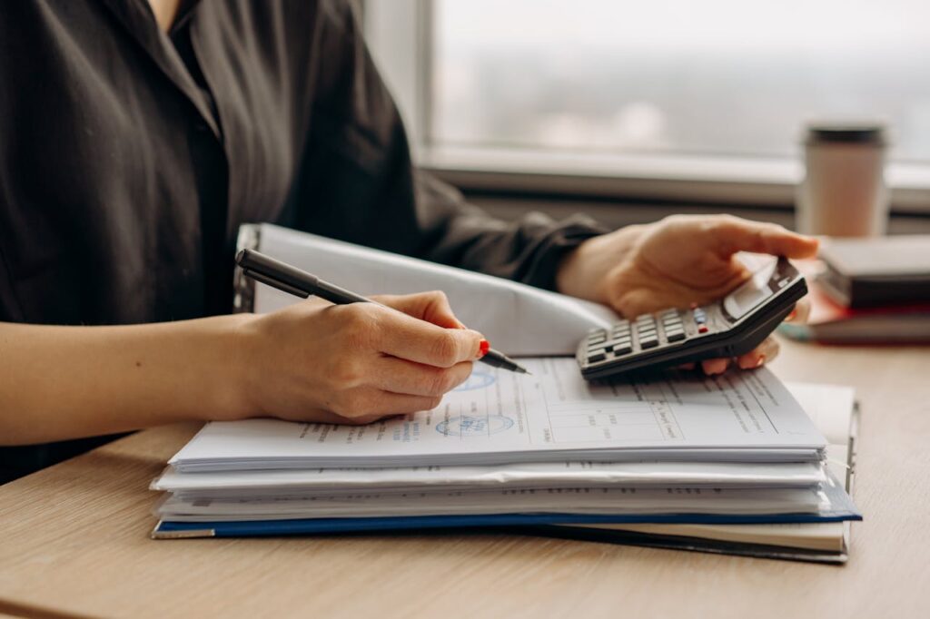 A woman is reviewing her finances to see if she can qualify for jumbo loans using documents and a calculator.