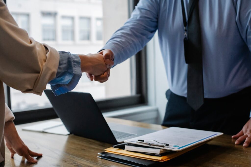 Two people are shaking hands over a desk after closing a P&L loan deal. 