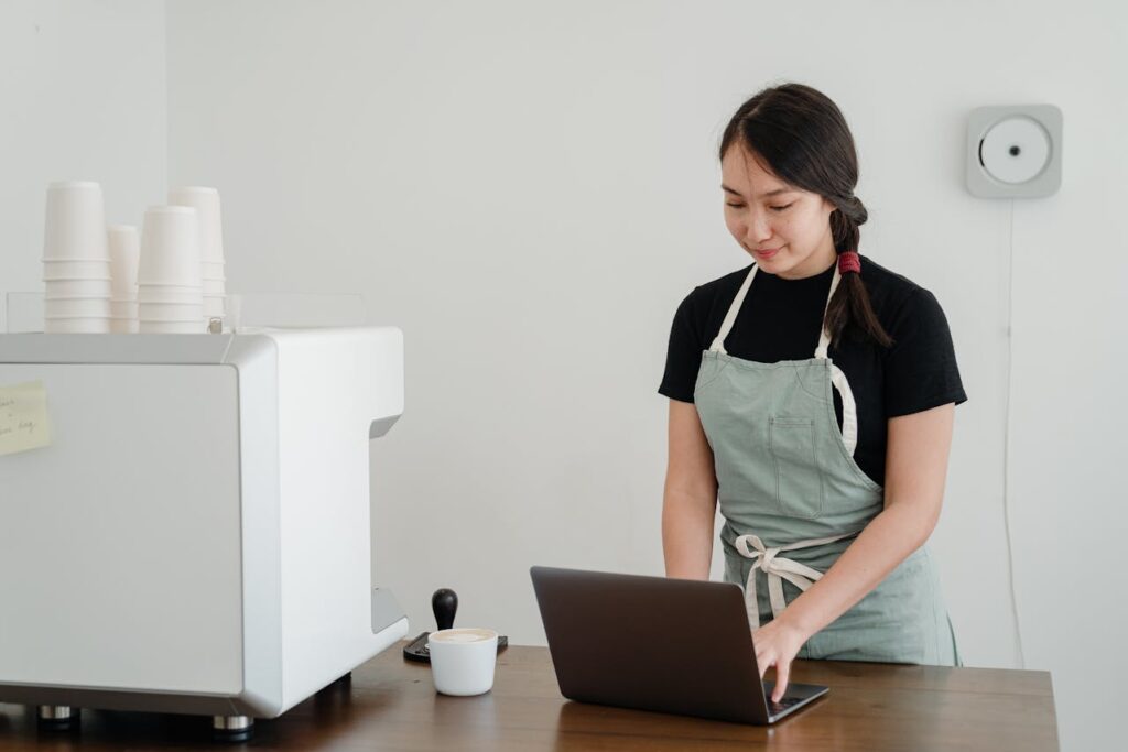 A cafe owner is applying for a Texas P&L loan on her laptop next to an espresso machine.