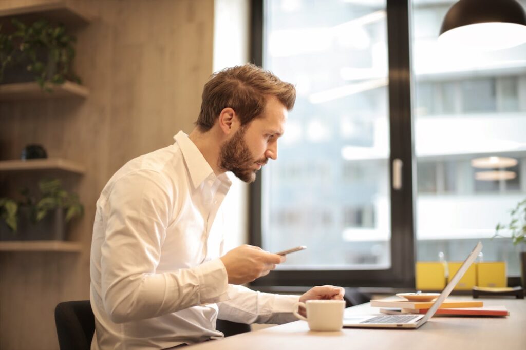 A real estate investor is looking at his phone and laptop to review his rental property mortgage loan options.