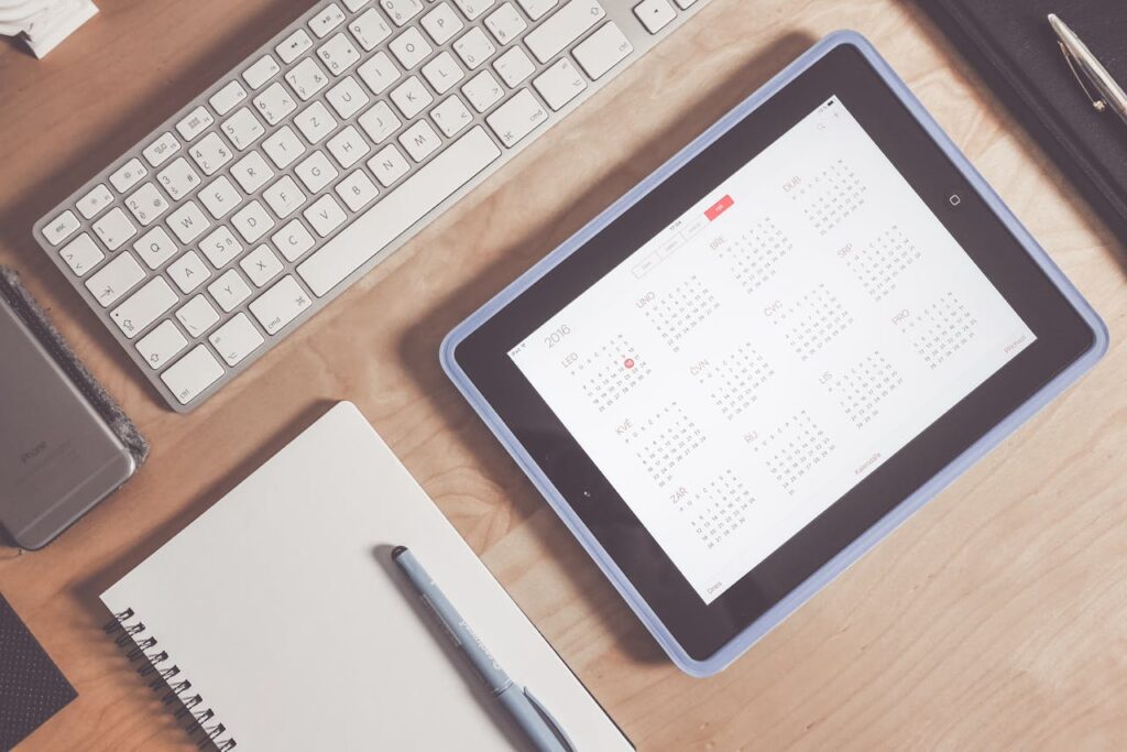 A top-down view of a desk with a keyboard, notebook, and an iPad with a calendar to determine a DSCR cash-out refinance timeline.