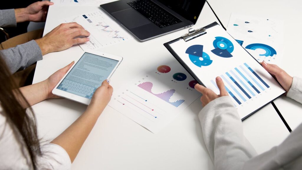 Three investors are gathered around a table with a laptop and charts to plan their goals with DSCR loans for property investment. 