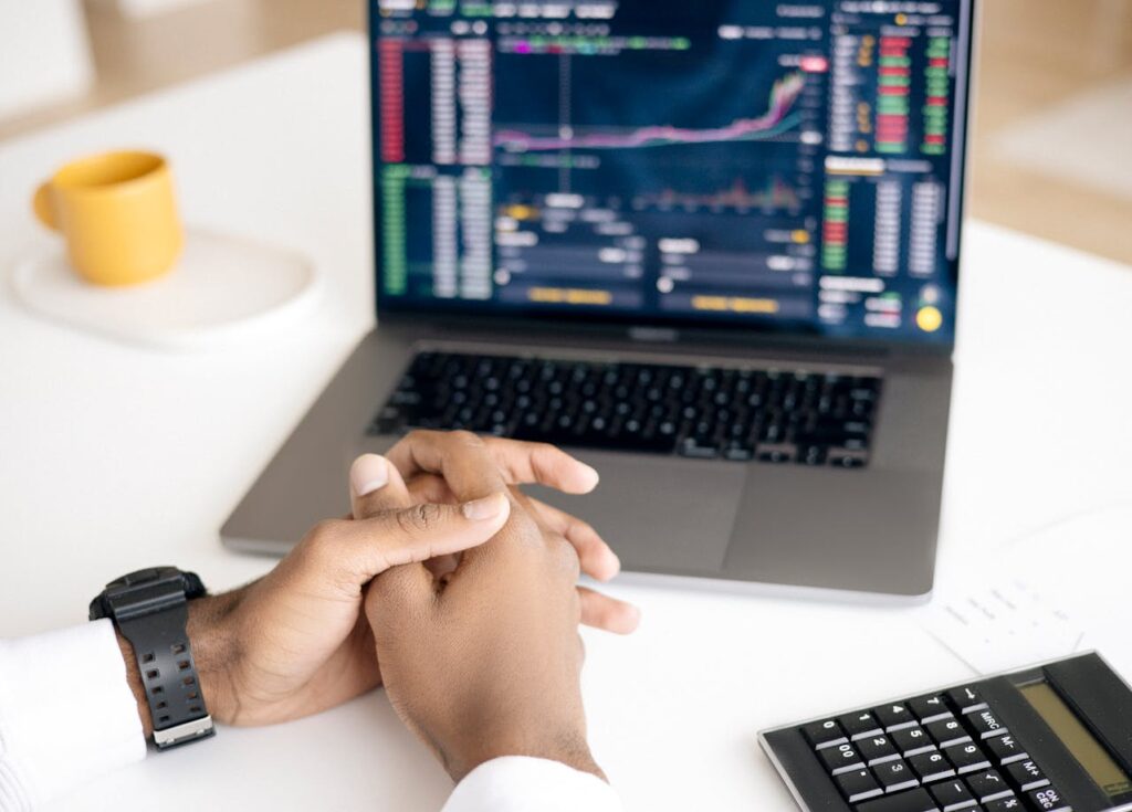 A person has their hands folded while looking at interest rates on their laptop. 