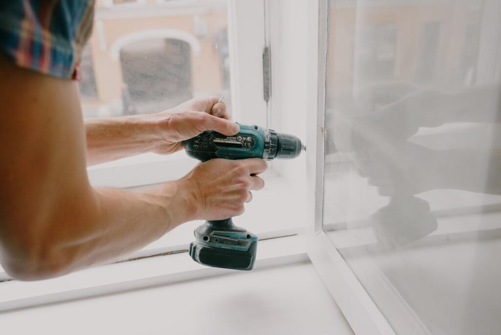 A person is drilling a screw into a windowsill to fix an issue that came up in the home inspection report.