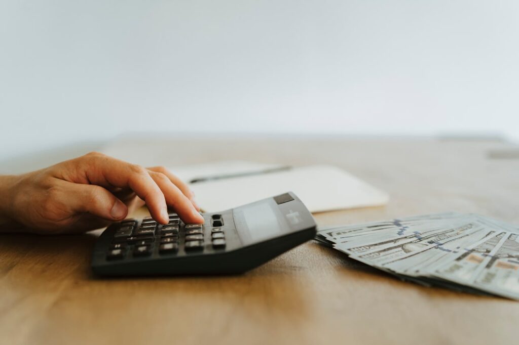 A person typing numbers into a calculator with hundred-dollar notes in front, checking to see if they meet the DSCR loan Maine requirements. 