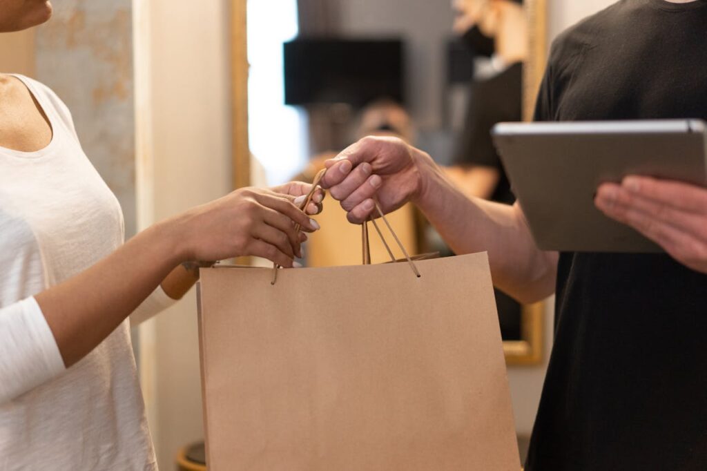 A shop owner is handing a shopping bag to a customer after a purchase. 