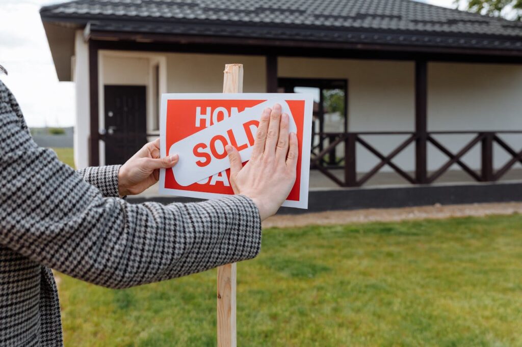 A realtor is putting up a "sold" sign on a house after explaining to her clients how to prove income when self employed. 