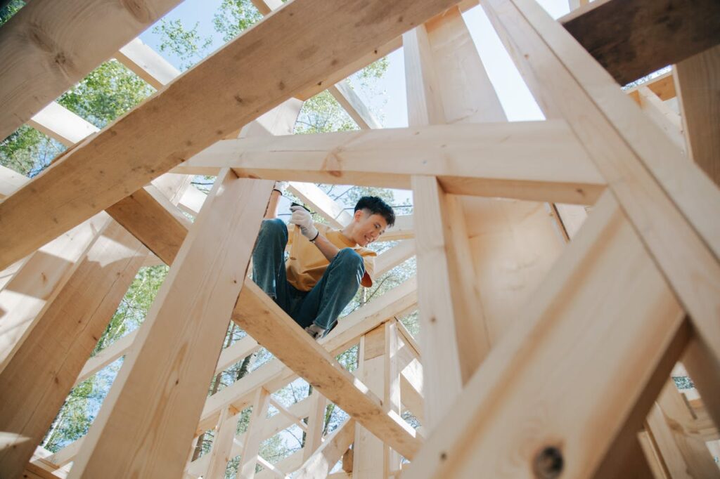 A handyman is standing on a wood beam of a home that's under construction. 