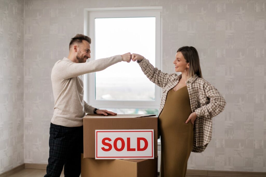 A pregnant couple is fist bumping after closing on their new home that was purchased with an FHA loan application. 