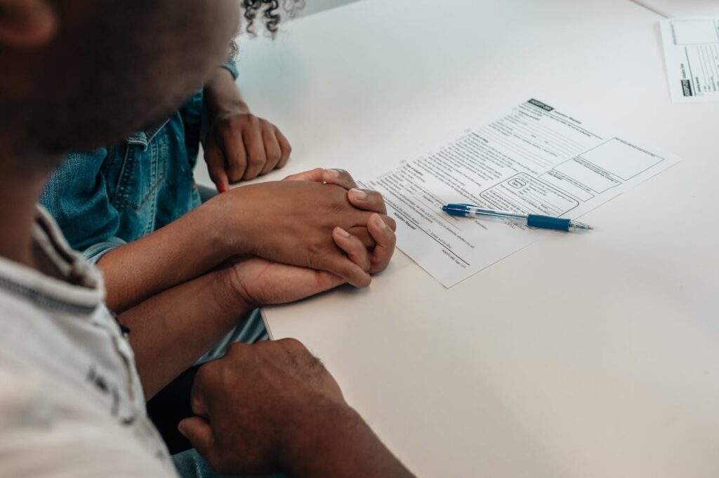 A couple is holding hands while signing a mortgage document that lists one spouse as a co-signer. 