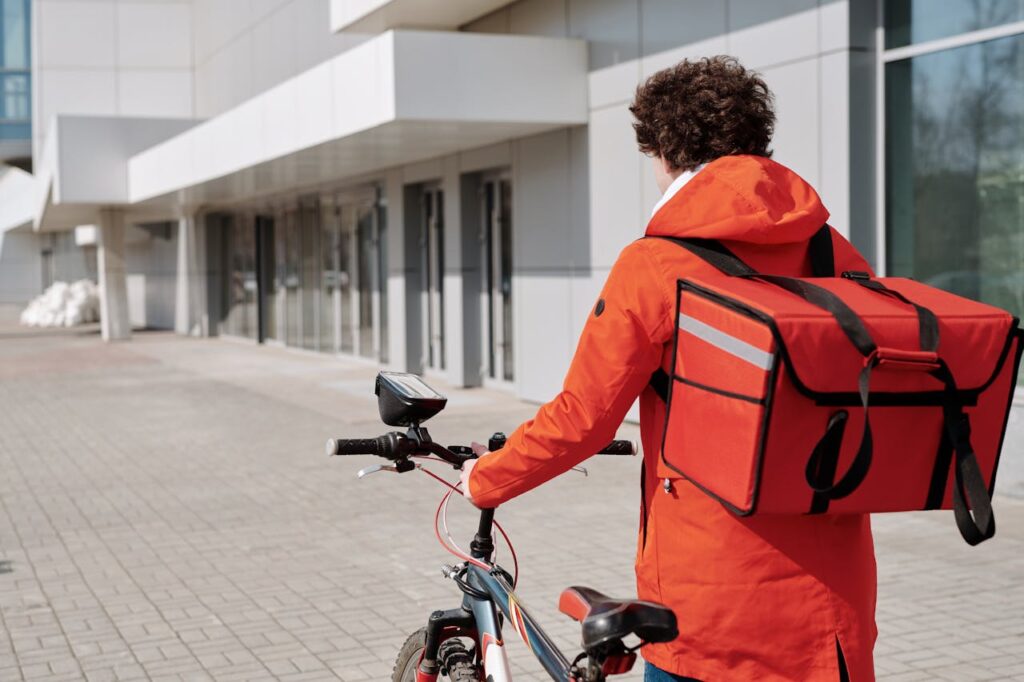 A delivery man in an orange jacket with his bike. 