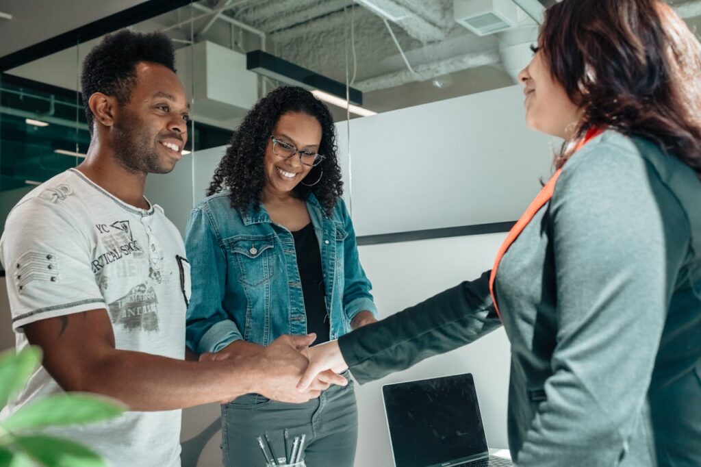 A couple is smiling while shaking a loan officer's hand after negotiating their rates, terms, and fees. 